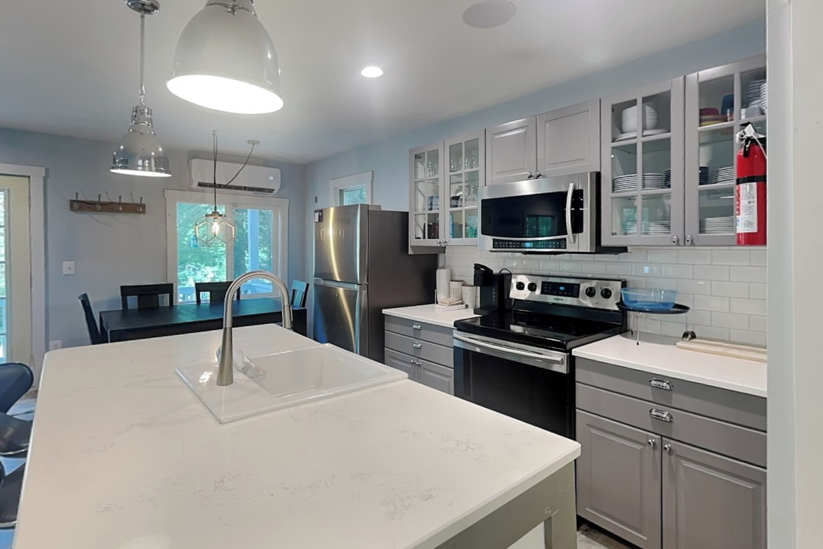 A modern kitchen with stainless steel appliances, a white countertop, and a dining area with a table and chairs.