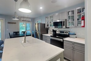 A modern kitchen with stainless steel appliances, a white countertop, and a dining area with a table and chairs.
