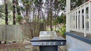 Ein schwarzer Grill für den Außenbereich mit Bedienfeld, vor einer Holzzaun und Bäumen.
