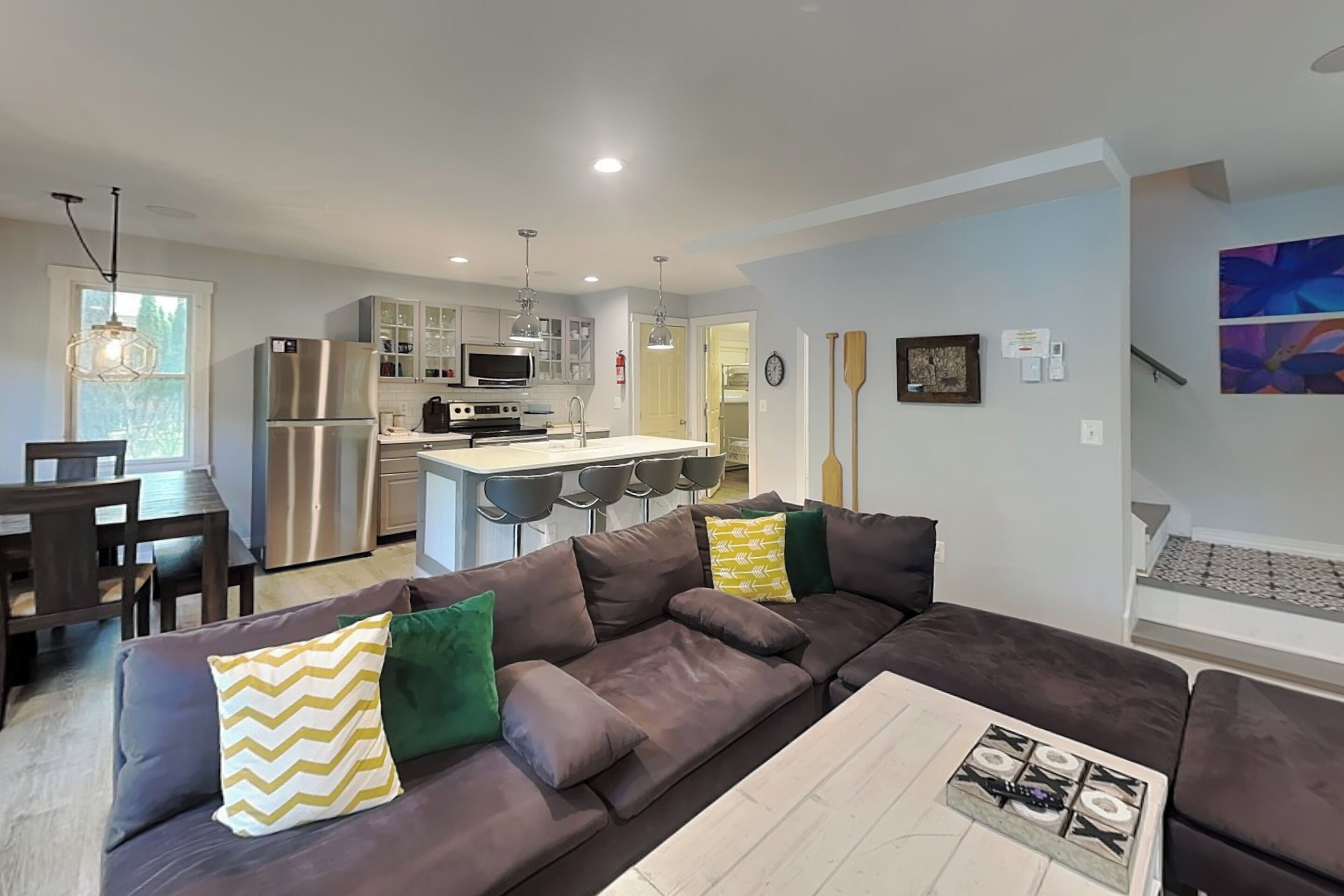 A modern kitchen with stainless steel appliances, a dining area with a dark wood table and chairs, and a living room with a large brown sectional sofa.