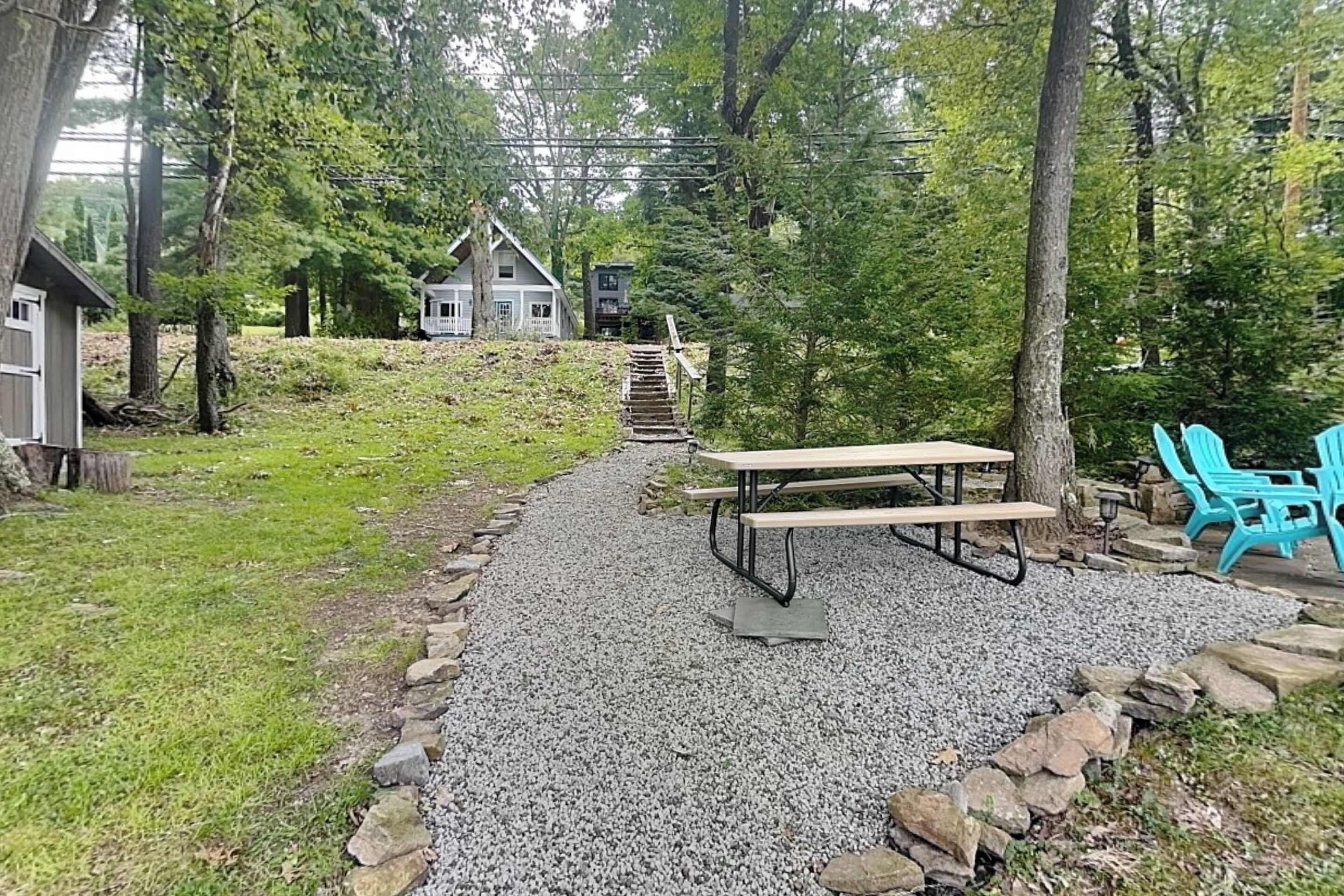 A gravel path leading to a picnic table with benches, surrounded by trees and a small shed.