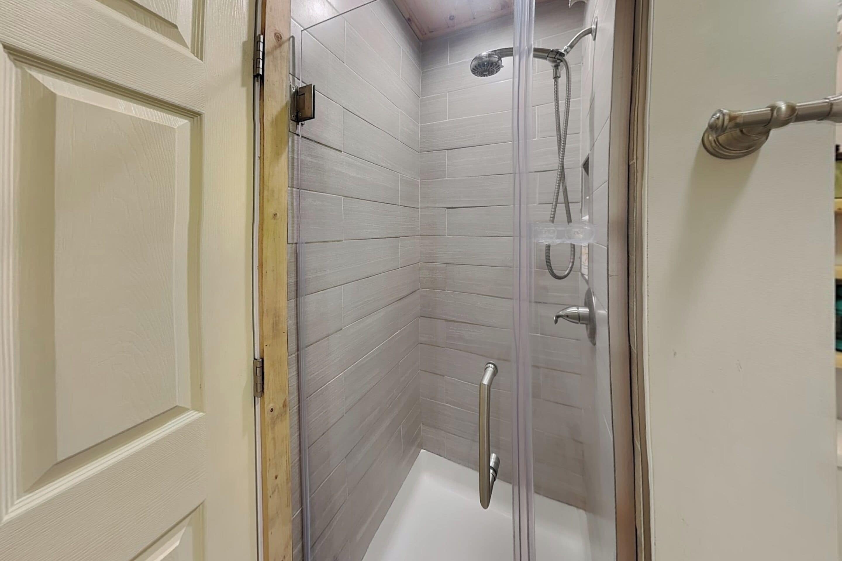 A corner shower with a glass door, a handheld showerhead, and a handheld shower attachment.