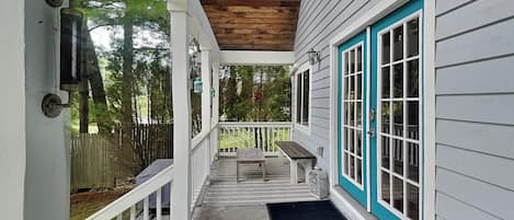 A covered porch with a wooden ceiling, a bench, and a door with a teal frame.