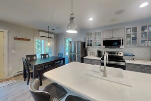 A modern kitchen with a central island, stainless steel appliances, and a dining area with a wooden table and chairs.
