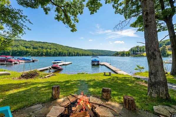 A lakeside view with a fire pit, docked boats, and a grassy area.