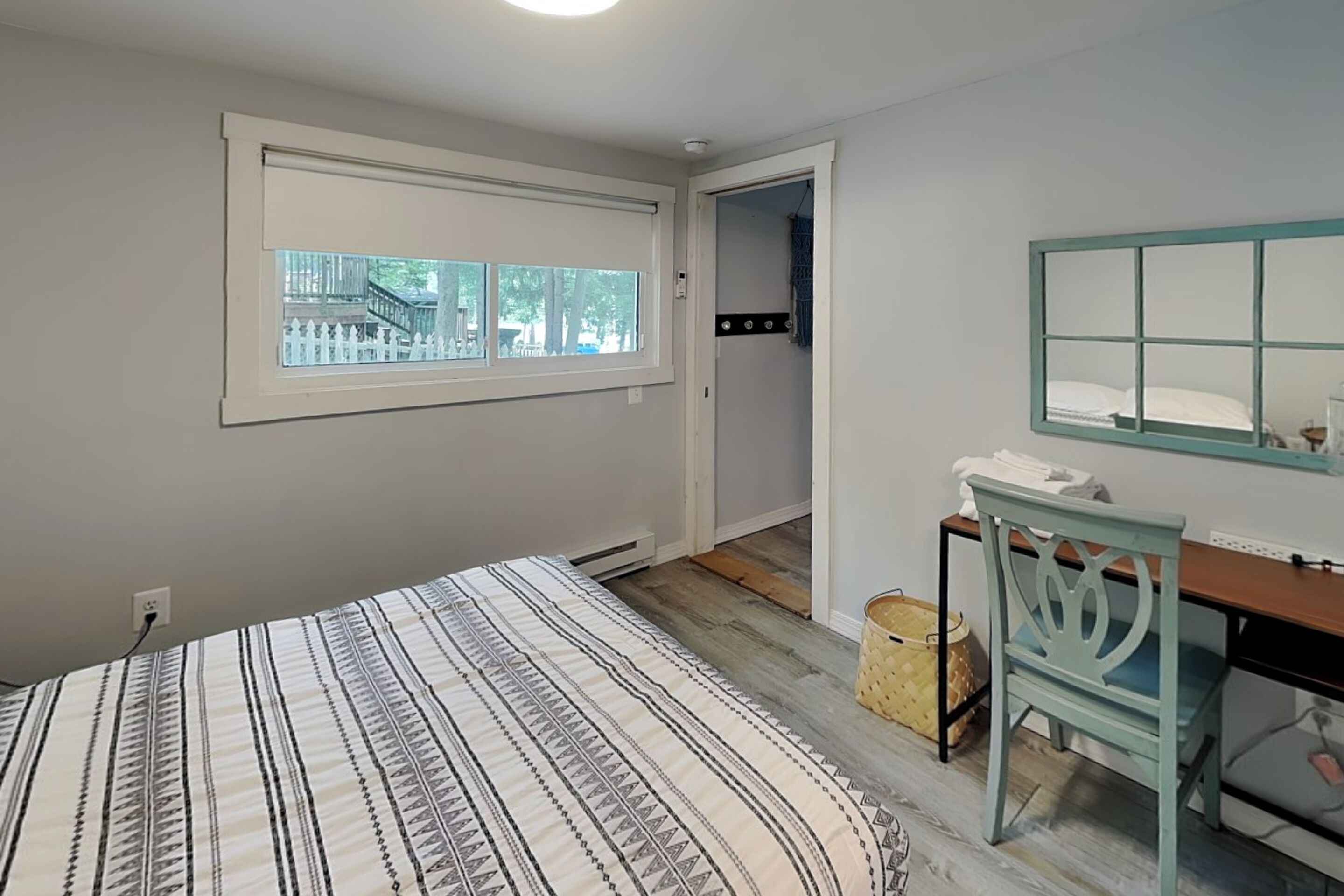 A bedroom with a bed, a desk, a chair, a window, and a door leading to a bathroom.