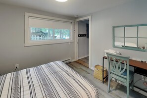 A bedroom with a bed, a desk, a chair, a window, and a door leading to a bathroom. - Winter Green Lodge (McHenry)