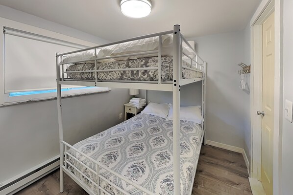 A bunk bed with a patterned bedspread, a bedside table with a lamp, and a window with a view of the outside.