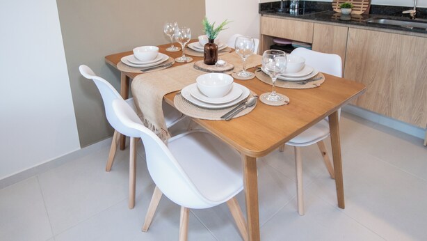 A dining table set with white plates, bowls, and cutlery, surrounded by white chairs. - Corporate Stays First del Sol - 202 (Asunción)
