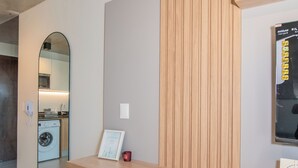 A modern room with a wooden desk, a white chair, a washing machine, and a mirror reflecting a kitchen area. - Corporate Stays First del Sol - 202 (Asunción)