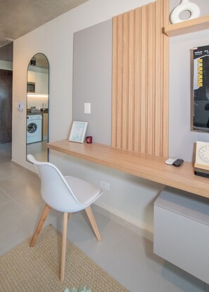 Una habitación moderna con un escritorio de madera, una silla blanca, una lavadora y un espejo que refleja una zona de cocina.
