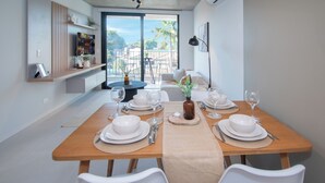 A dining area with a wooden table set for four, white chairs, and a view of the outdoors through large windows. - Corporate Stays First del Sol - 202 (Asunción)