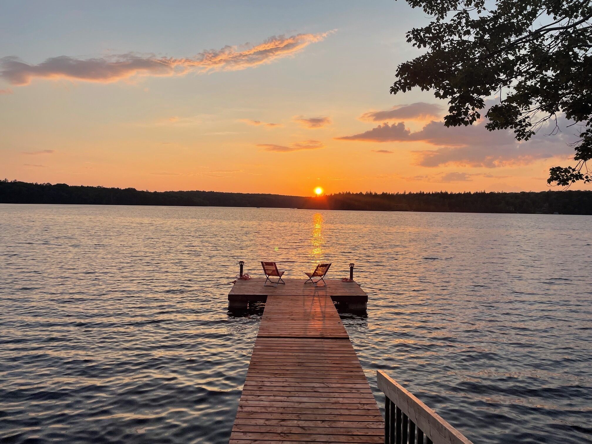 A wooden pier extending into calm water with a sunset in the background.
