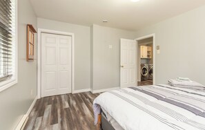 Un dormitorio con cama, armario, puerta que da a un cuarto de lavado y ventana con persianas.