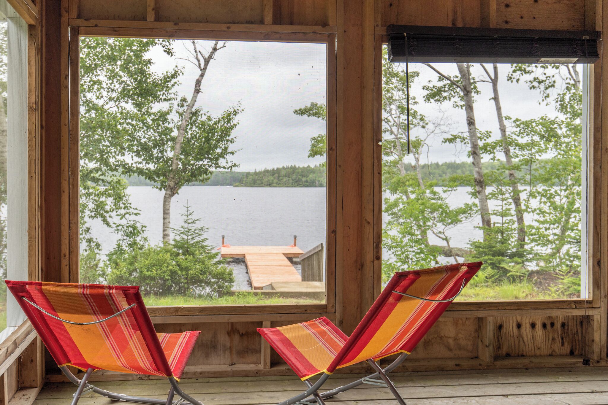 A wooden cabin with two striped chairs facing a lake view.