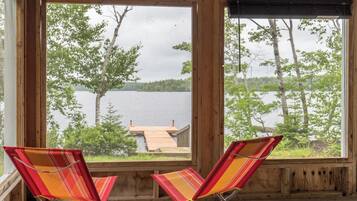 A wooden cabin with two striped chairs facing a lake view.