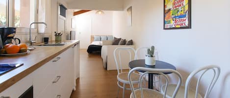 A modern kitchen with a built-in oven, a dining area with a table and chairs, and a bedroom with a bed and a window.