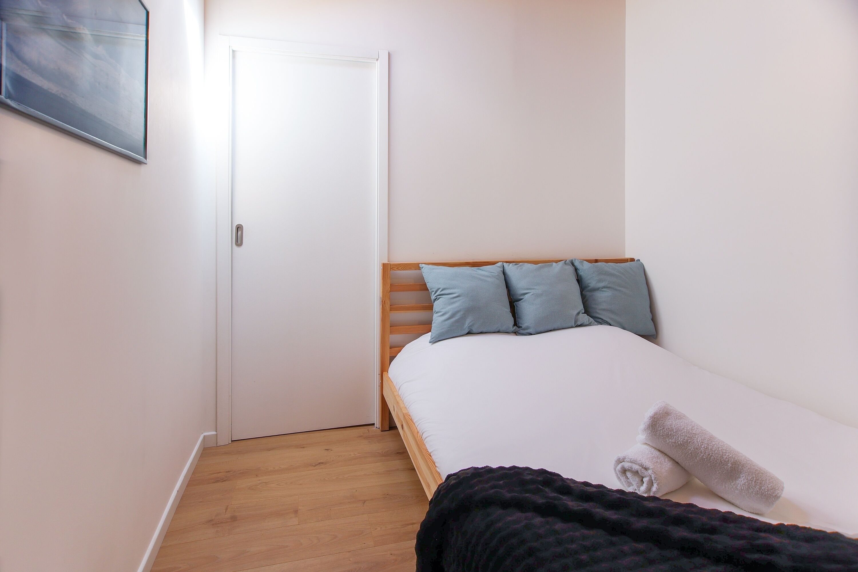 Une petite chambre avec un lit simple, une tête de lit en bois, une porte blanche et un plancher en bois.