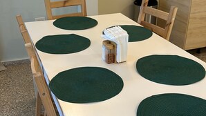 A dining table with a white tablecloth, surrounded by wooden chairs, and green placemats. - 2BR Luquillo Home Near Beach & El Yunque, A/C + Parking (Luquillo)