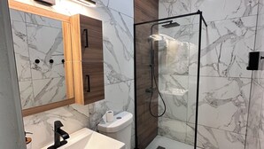 A modern bathroom with a marble backsplash, a wooden vanity, a white sink, a toilet, and a glass-enclosed shower. - 2BR Luquillo Home Near Beach & El Yunque, A/C + Parking (Luquillo)