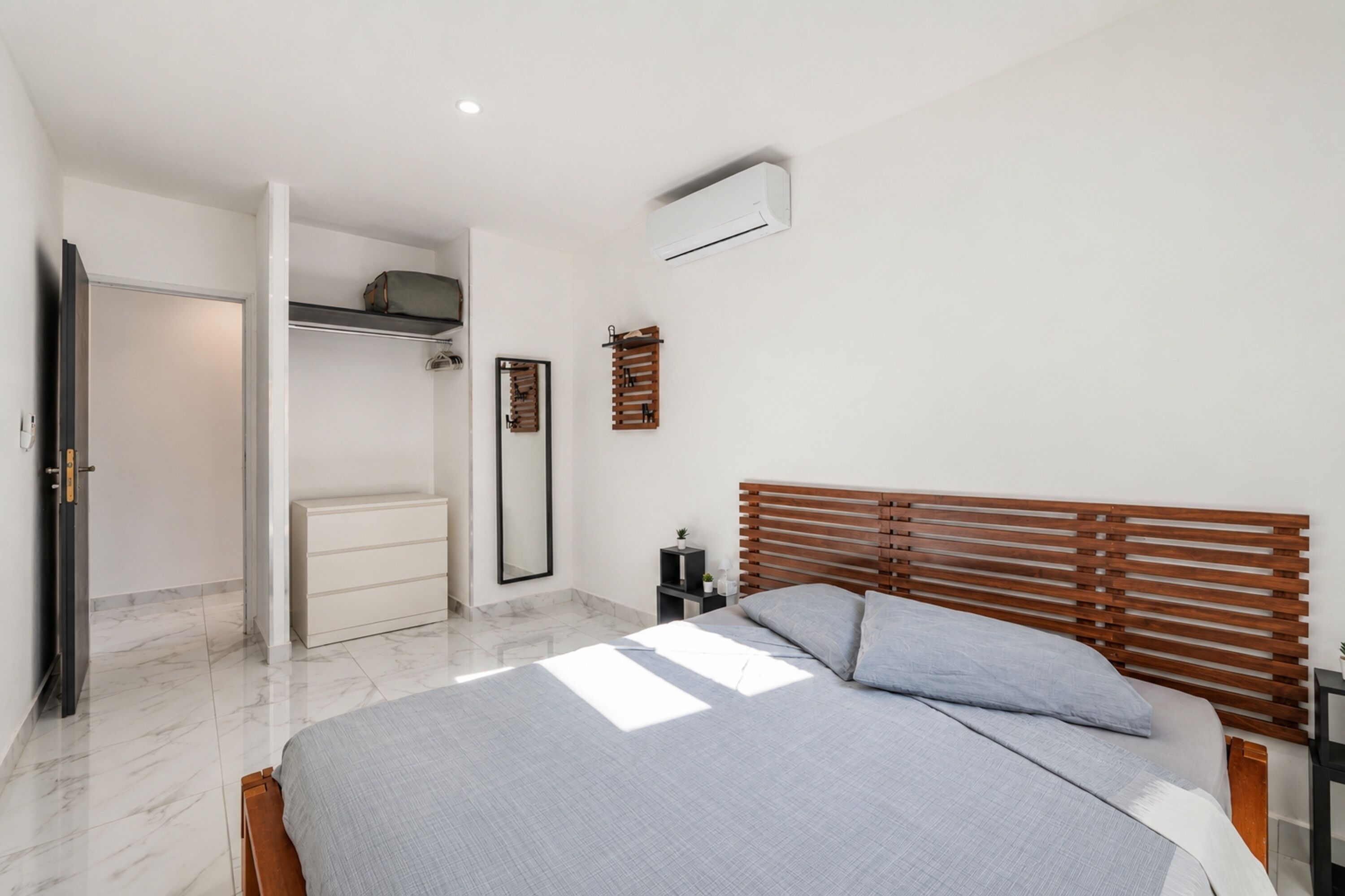 Une chambre à coucher comprenant un lit, une armoire, un miroir et un climatiseur fixé au mur.