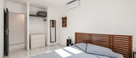 Une chambre à coucher comprenant un lit, une armoire, un miroir et un climatiseur fixé au mur.