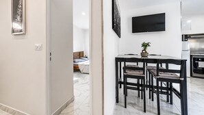 Una camera d'albergo moderna con un letto, un'area pranzo con sedie, una TV a parete e un angolo cottura.