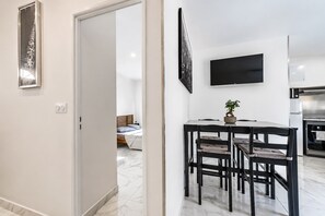 A modern hotel room with a bed, a dining area with chairs, a TV mounted on the wall, and a kitchen area. - Chez Frédéric et Josiane - Bel appt avec terrasse (Montpellier)