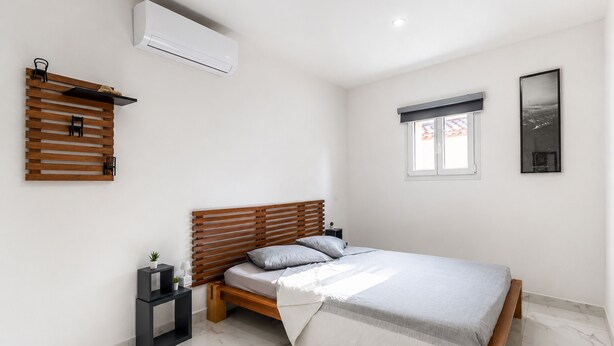 Una camera da letto con un letto di legno, un comodino, una mensola a parete, una finestra con vista e un condizionatore d'aria.