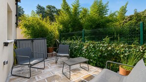 Un patio esterno con tavolo e sedie, circondato da un recinto verde e vegetazione lussureggiante.