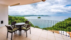 Ein Balkon mit Tisch und Stühlen, einem Deckenventilator und Blick auf ein Gewässer mit grüner Landschaft und entfernten Inseln.