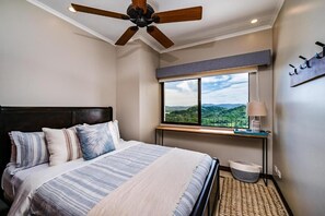A bedroom with a bed, a ceiling fan, a window with a view, and a bedside table with a lamp. - Stylish Oceanview Condo with Quick Beach Access, Modern Design & Spacious Balcony (Santa Cruz)