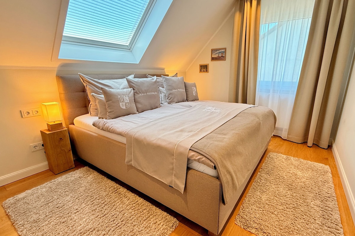 Un dormitorio con cama, mesita de noche, lámpara, ventana con persianas y vistas al exterior.