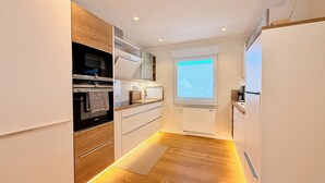 Eine moderne Küche mit eingebauten Geräten, Holzschränken und einem Fenster mit Jalousien.