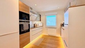 Una cocina moderna con electrodomésticos integrados, armarios de madera y un ventanal con persianas.