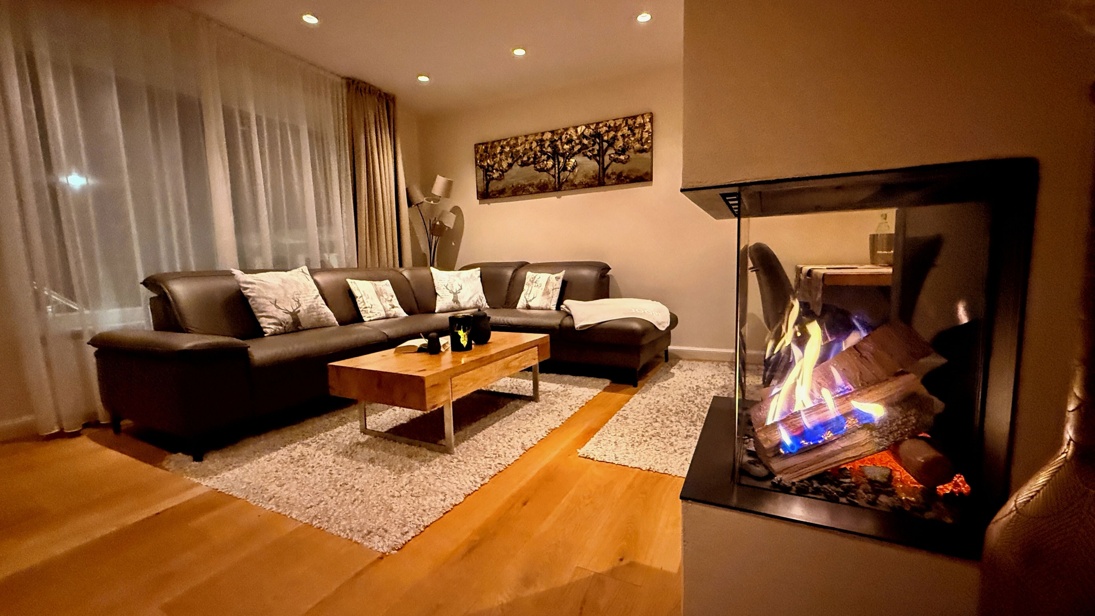 Un salon comprenant un ensemble de canapés, une table basse, une cheminée avec un feu de bois et un tableau accroché au mur.