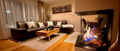 Un salon comprenant un ensemble de canapés, une table basse, une cheminée avec un feu de bois et un tableau accroché au mur.