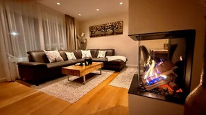 Una sala de estar con un sofá, una mesa de centro, una chimenea encendida y un cuadro en la pared.
