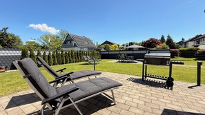 A backyard with a barbecue grill, two lounge chairs, and a paved patio area. - Haus-Holiday.de - Walkenried (Walkenried)