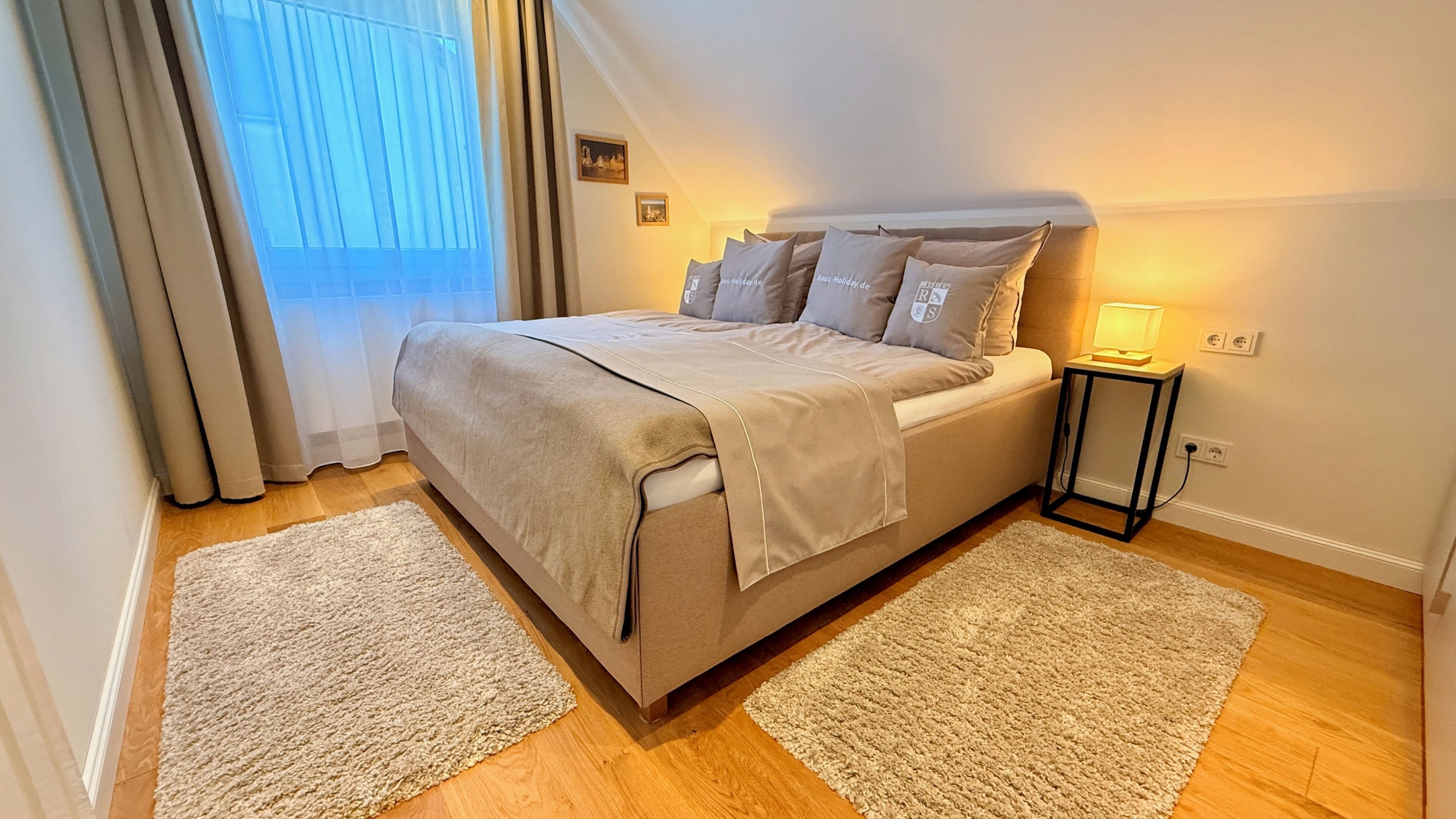 Un dormitorio ordenado con una cama, dos mesitas de noche y una ventana con cortinas.