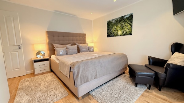 Un dormitorio con cama, mesitas de noche, una silla y un cuadro en la pared.
