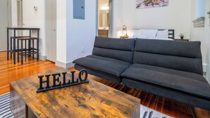 Ein modernes Wohnzimmer mit einem dunklen Sofa, einem Couchtisch aus Holz mit der Aufschrift 'HELLO', einem kleinen Beistelltisch und einem Gemälde an der Wand.