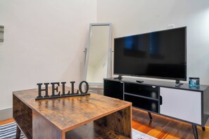 A room with a wooden table, a black 'HELLO' sign, a flat-screen TV, and a black cabinet. - Large Studio - Nearby Parking - Hospitals - 3F (Louisville)