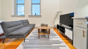 Ein modernes Wohnzimmer mit einem grauen Sofa, einem Holztisch mit der Aufschrift 'HELLO', einem Flachbildfernseher und einem weißen Schrank.