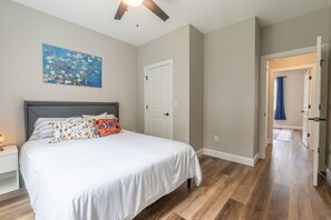 Een slaapkamer met een bed, nachtkastje, plafondventilator, deur en een gang naar een andere kamer.