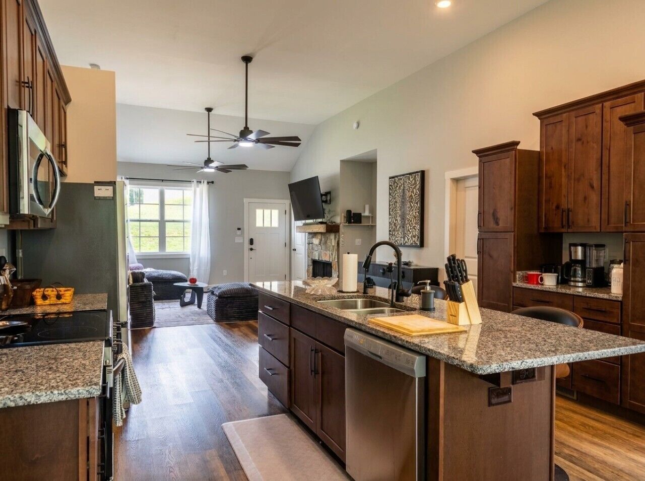 A kitchen with a central island, wooden cabinets, a ceiling fan, and a view to the living area.