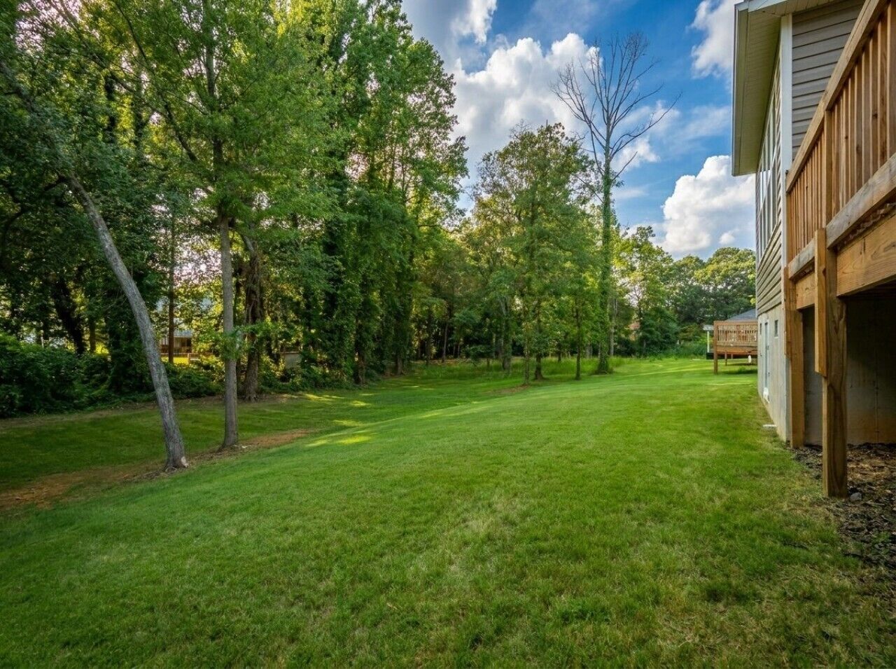 A backyard with a lawn, trees, and a wooden deck.