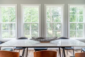 Comedor con una mesa grande y sillas, ventanas amplias con vistas a árboles y una decoración central.