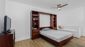 A bedroom with a bed, a TV, a ceiling fan, and built-in shelving. - Station Square Condominiums – Spacious Downtown Clearwater Retreat with Resort-Style Amenities (Clearwater)