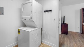 A laundry room with a front-loading washer and dryer, a wooden cabinet, and a wall-mounted drying rack. - Station Square Condominiums – Spacious Downtown Clearwater Retreat with Resort-Style Amenities (Clearwater)